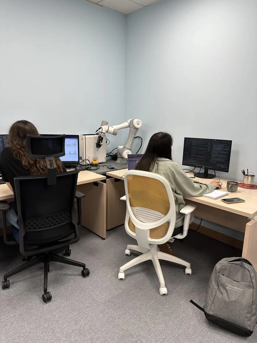 Dos personas del equipo trabajando en sus puestos junto al brazo robótico colaborativo